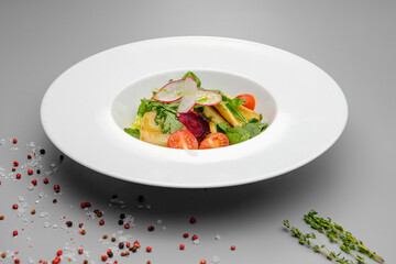 Squid with vegetables, tomatoes, salad and radishes on a white plate.
