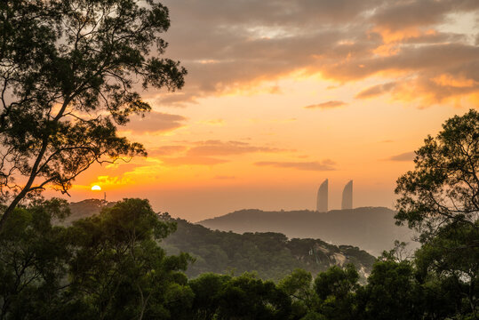 Spectacular scenery of green hills and silhouettes of modern skyscrapers of Xiamen city in China against cloudy evening sky during sunset time