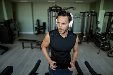 Fototapeta premium Young sportsman with headphones running on a treadmill in a gym.