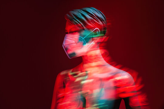 Plastic female dummy with naked chest and in protective mask showing concept of COVID 19 prevention while illuminated by neon light in long exposure