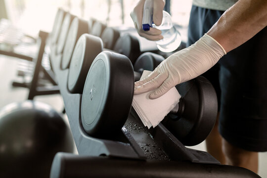 Close-up of athletic man cleaning dumbbells with disinfectant in a gym.