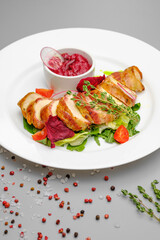 Chicken fillet in bacon with arugula and sauce on a white plate.