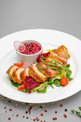 Chicken fillet in bacon with arugula and sauce on a white plate.