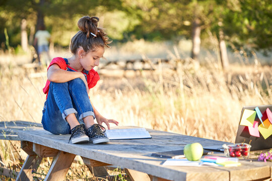 Ten-year-old girl on the field sitting at a wooden table, dressed in a red shirt and jeans