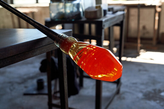 Side view of burning hot liquid glass mass on blowpipe in process of producing shisha glass base