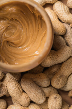 Top view of jar full of peanut butter placed on wooden table in kitchen with peanuts