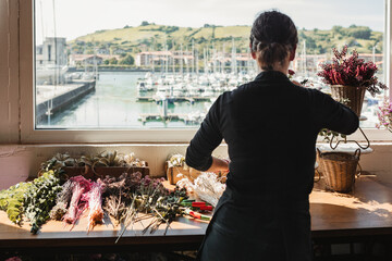 Back view of unrecognizable female florist in black uniform composing bouquets with assorted colorful flowers and decorating showcase of floristry store