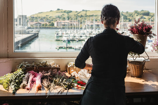 Back view of unrecognizable female florist in black uniform composing bouquets with assorted colorful flowers and decorating showcase of floristry store