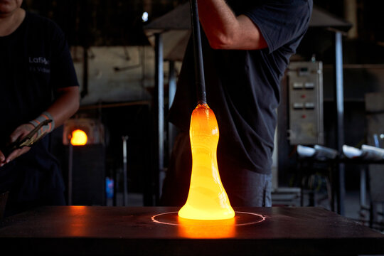 Crop men in workshop working piece of hot liquid glass while blowing glass detail