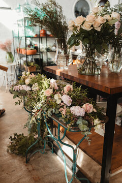 Gentle wedding floral composition with blooming pink roses arranged on metal stand near shelf with various bouquets in floristry store