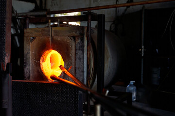 Blowpipe and melting glass in hot furnace in workshop