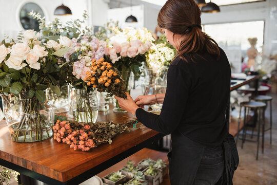 Side view of adult female floristry shop worker standing at wooden counter and arranging bouquets of fresh roses