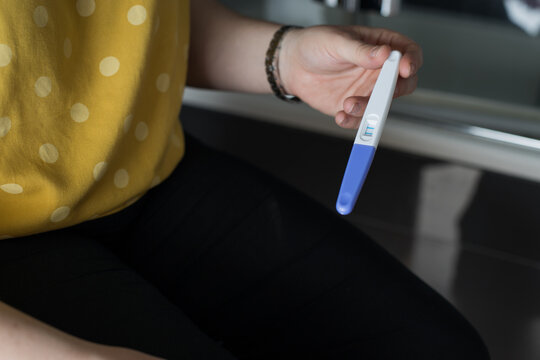 From above of crop unrecognizable female sitting holding pregnancy test with double bars