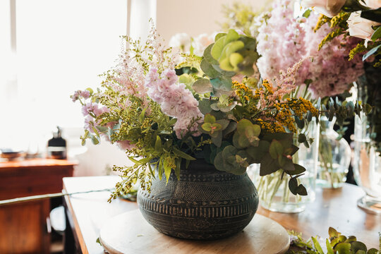Beautiful bouquet with various flowers including craspedia flowers with green eucalyptus branches arranged in ornamental ceramic pot placed on table in creative floristry studio