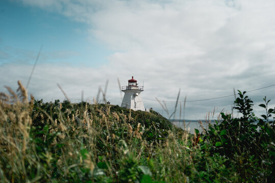 Famous Peggys Cove Lighthouse located on green cliff against cloudy sky on seashore in Canada
