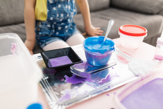 From above of crop anonymous kid in casual wear sitting on cozy sofa in front of table with dirty tray and plastic containers with bright blend at home