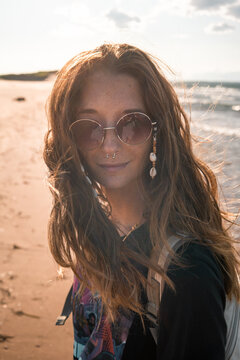 Calm female hippie with long hair standing on beach near sea on background of sunset