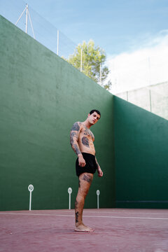 Side view od muscular male athlete with tattoos and naked torso standing resting during outdoors workout looking at camera