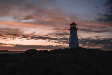 Peggys Cove Lighthouse located on stony coast against sea and cloudy sunset sky in evening in Canada
