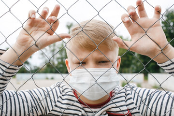 Boy in a medical mask isolated in a cage during a coronavirus epidemic. Concept of quarantine and protection from polluted air. illness, infection, virus, flu, COVID-19.