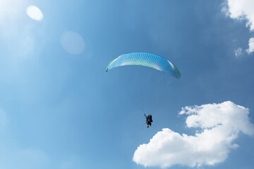Blue Paraglider flying into the sky with clouds in a sunny day