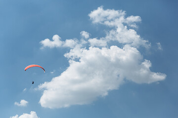 Blue Paraglider flying into the sky with clouds in a sunny day