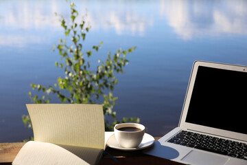 coffee cup, laptop and writing on the background of the sky and the river, remote work in the country