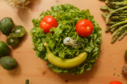 Naklejki From above composition of fruits and vegetables in shape of smiley face on table in kitchen