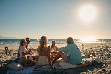 Mature male and female friends with girl enjoying dinner at beach picnic against sky during sunset. Riviera Nayarit, Mexico