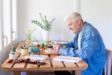 Senior man painting on table at home