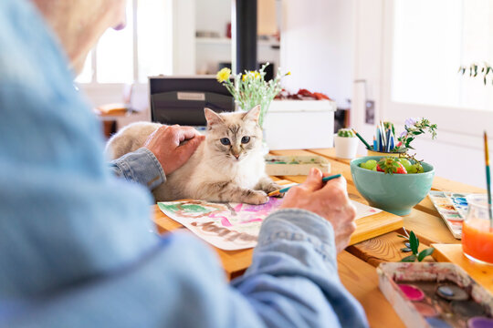 Senior man stroking cat while painting on paper at home