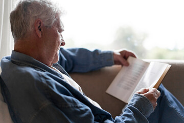 Senior man reading book while relaxing on sofa at home