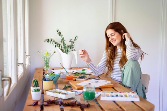 Happy Young Woman Painting With Watercolor Paints On Table At Home