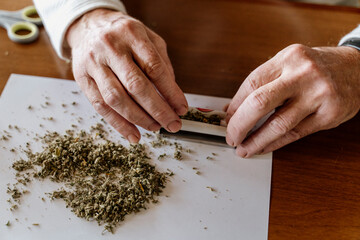 Close-up of retired senior man rolling weed on table