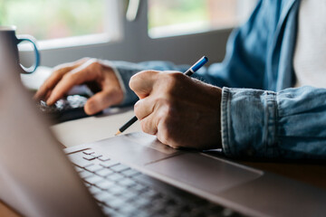 Cropped image of senior man using calculator and laptop while writing with pencil at home