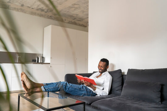 Smiling man sitting on couch in modern apartment reading a book