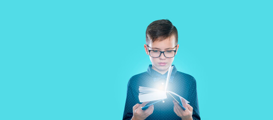 Little cheerful school boy wearing glasses holding a book over blue background. Back to school concept