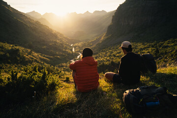 Fototapeta premium Two young men sitting on the grass watching the sunset on top of a valley in Pyrenees
