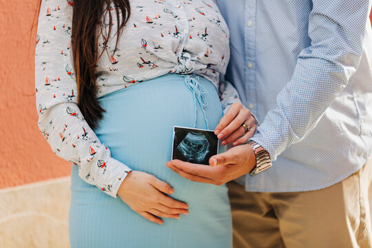 Expectant couple holding ultrasound photo while standing outdoors