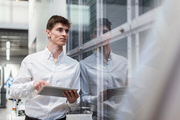 Businessman holding digital tablet examining production through glass in factory