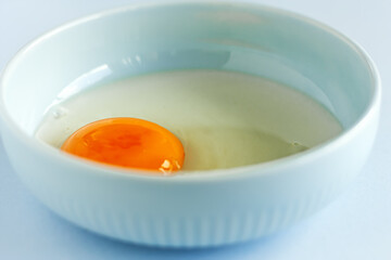 Fresh organic raw yolk and white of egg in light blue bowl on pastel background. Healthy breakfast and fresh ingredients. Selective focus