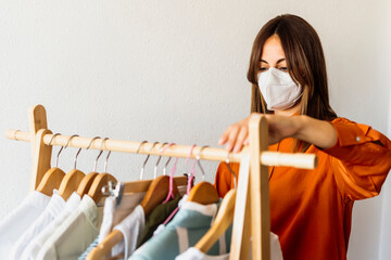 Female fashion designer working at home with clothes stand wearing protective face mask