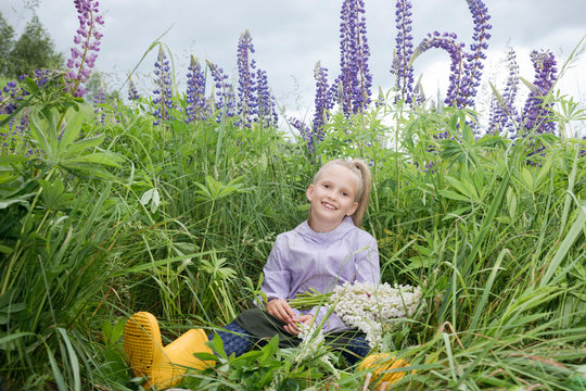 Portrait of happy girl sitting in front of lupine field with bunch of picked flowers