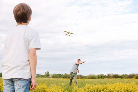Father and son playing with toy airplane on rape field against sky - Powered by Adobe