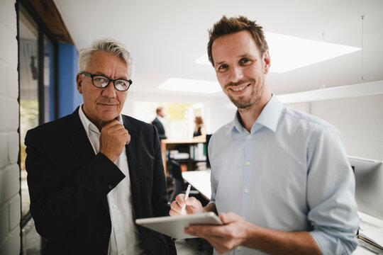 Two successful businessmen standing in office, using digital tablet