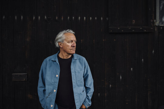 Senior man standing at wooden wall looking sideways