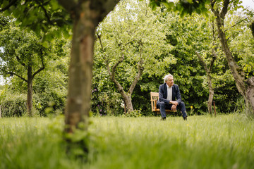 Senior businessman sitting on a chair in a rural garden
