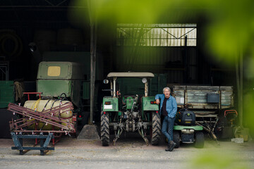 Confident senior man on a farm with tractor in barn