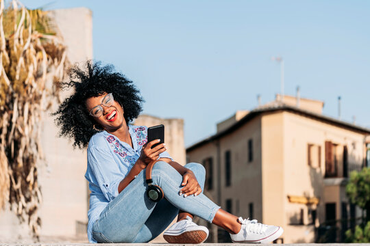Laughing woman with afro hair and glasses using smartphone