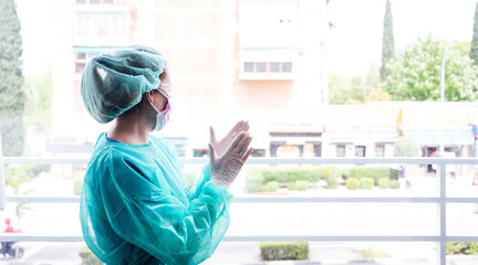 Female nurse wearing protective workwear clapping hands at window in hospital